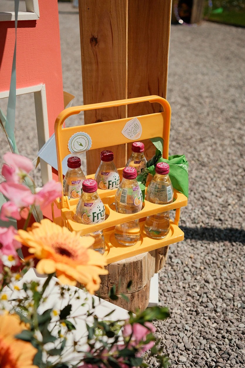 camp-ana-decoration-boissons-personnalisees Présentoir jaune contenant des bouteilles de jus de fruits, intégré à la décoration colorée de l’événement Camp ANA.