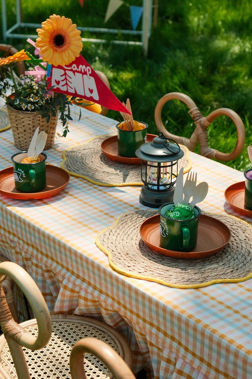 camp-ana-decoration-table-evenement-enfants-converti-depuis-jpg Scénographie de table Camp ANA en plein air avec vaisselle personnalisée, nappes à carreaux, fleurs, fanions et accessoires de camping.