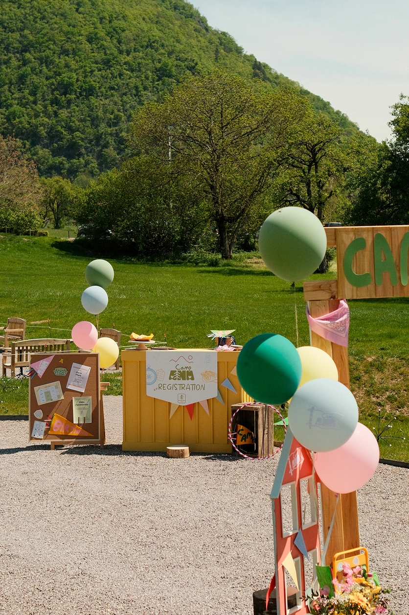 camp-ana-espace-accueil-evenement-enfants Espace d’accueil de l’événement Camp ANA en plein air, avec comptoir d’inscription, signalétique personnalisée et ballons pastel.