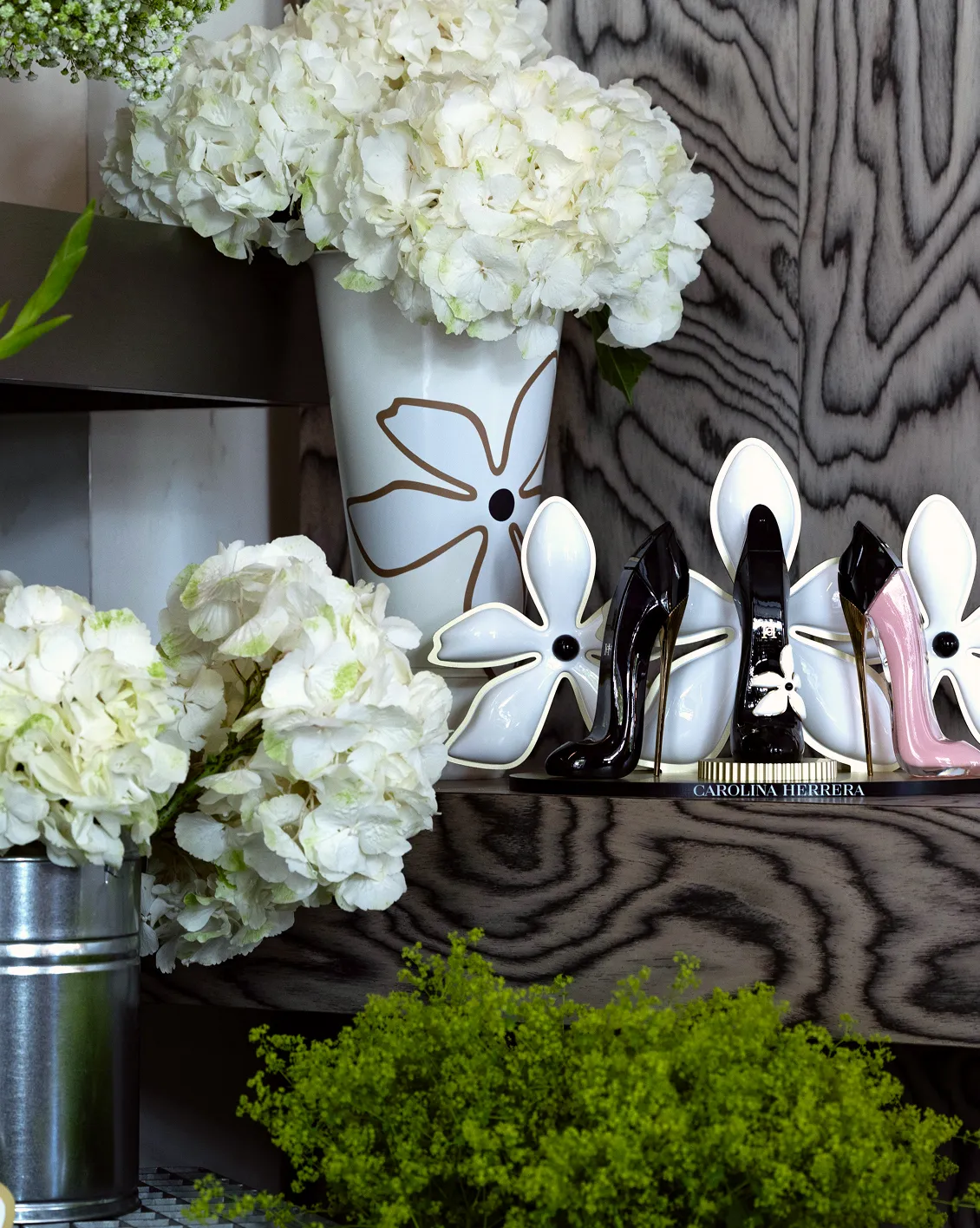 carolina-herrera-good-girl-decoration-florale-converti-depuis-jpg Mise en scène des parfums Good Girl de Carolina Herrera avec escarpins miniatures, fleurs blanches, vases personnalisés et décor en bois texturé.