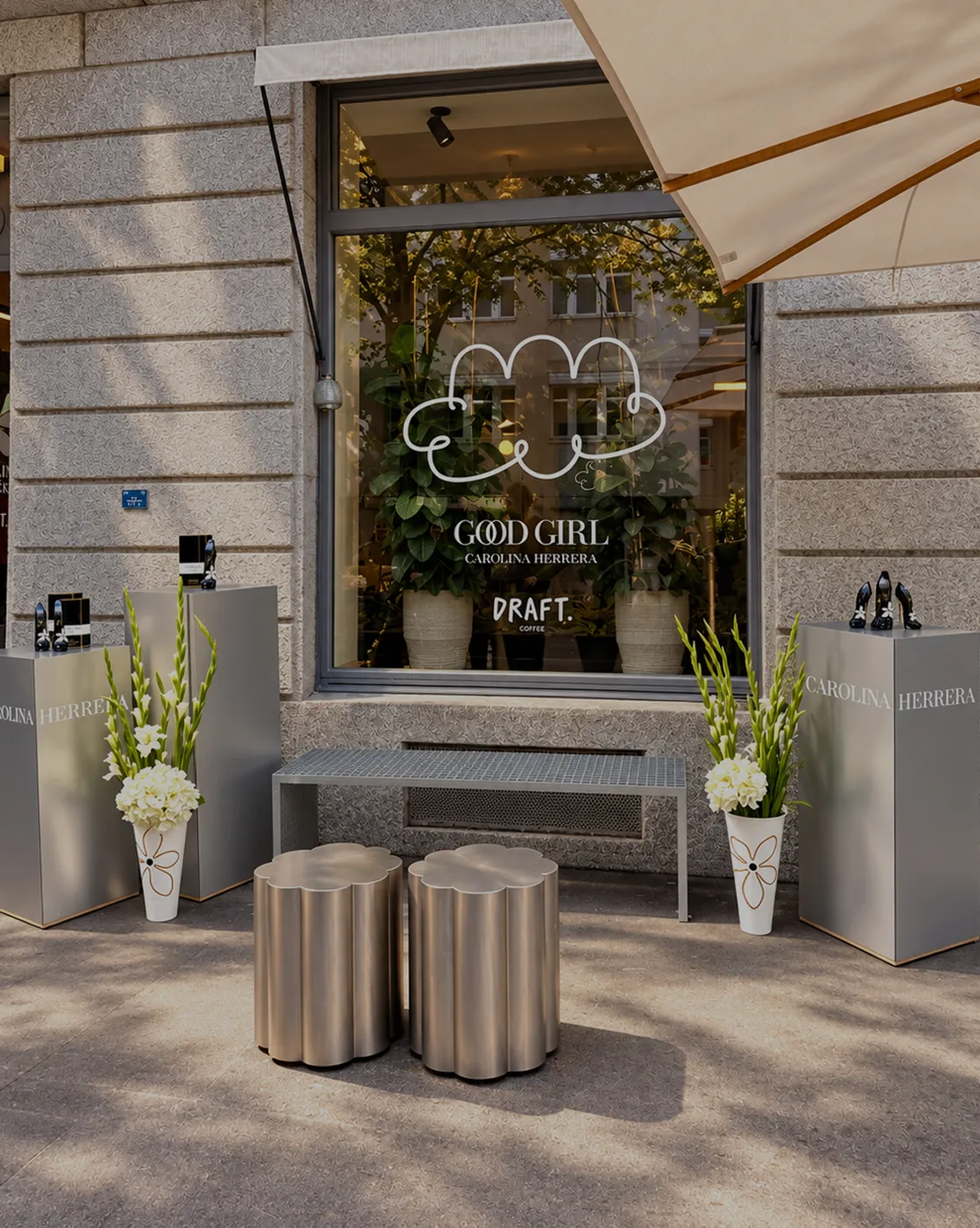 carolina-herrera-good-girl-scenographie-evenementielle-converti-depuis-jpg Scénographie événementielle Carolina Herrera Good Girl devant une vitrine, avec présentoirs argentés, compositions florales blanches et mobilier design.