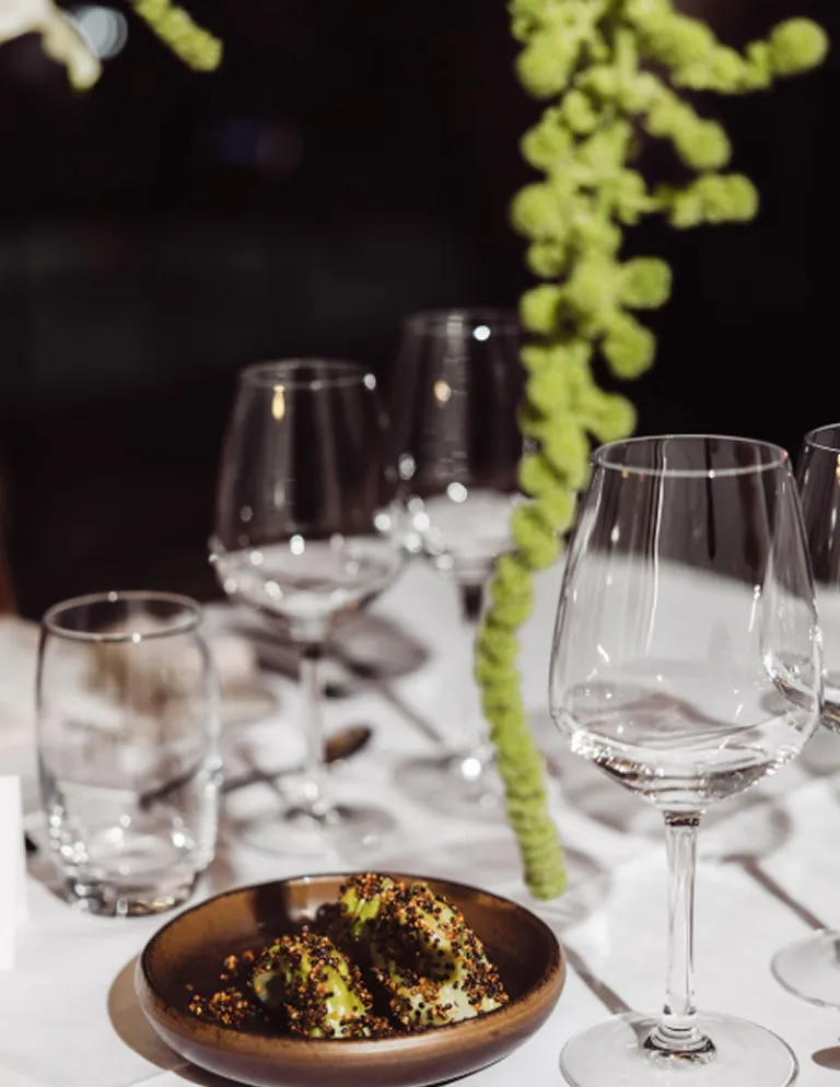 radis-decoration-table-evenement-sur-mesure-converti-depuis-jpg Détail d’une table dressée pour un événement Radis, avec verres à vin, vaisselle artisanale et composition végétale suspendue.