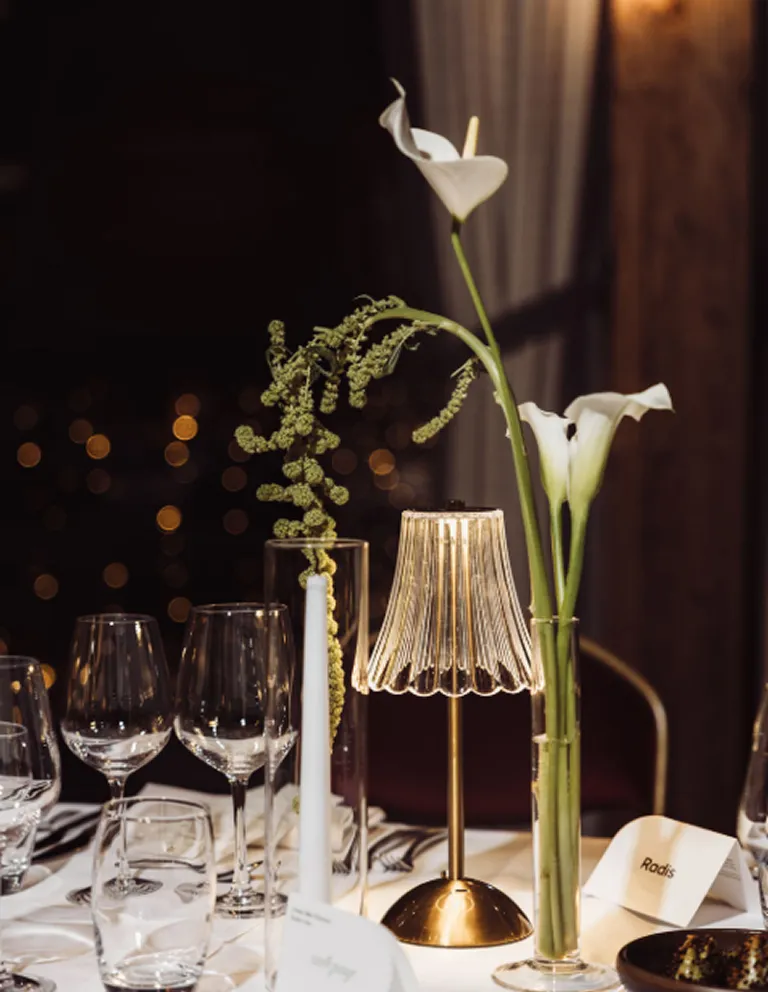 radis-scenographie-table-evenement-professionnel-converti-depuis-jpg Scénographie de table pour un événement Radis, avec compositions florales blanches, verrerie élégante et lampe dorée.