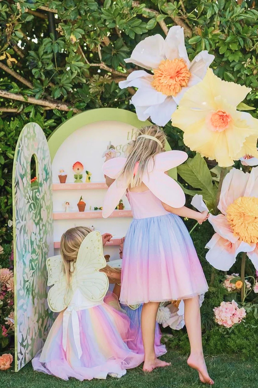 scenographie-enfants-univers-feerique-yma Deux enfants déguisées en fées découvrent un décor immersif composé de fleurs géantes et d’un espace de jeu miniature.