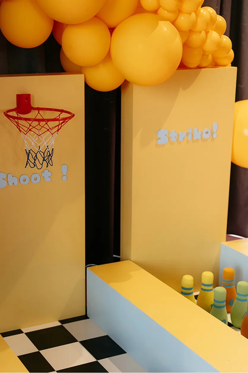 scenographie-espace-jeux-enfants-basket-bowling-yma-converti-depuis-jpg Espace de jeux pour enfants avec panier de basket, quilles de bowling, décor jaune sur mesure et arche de ballons.