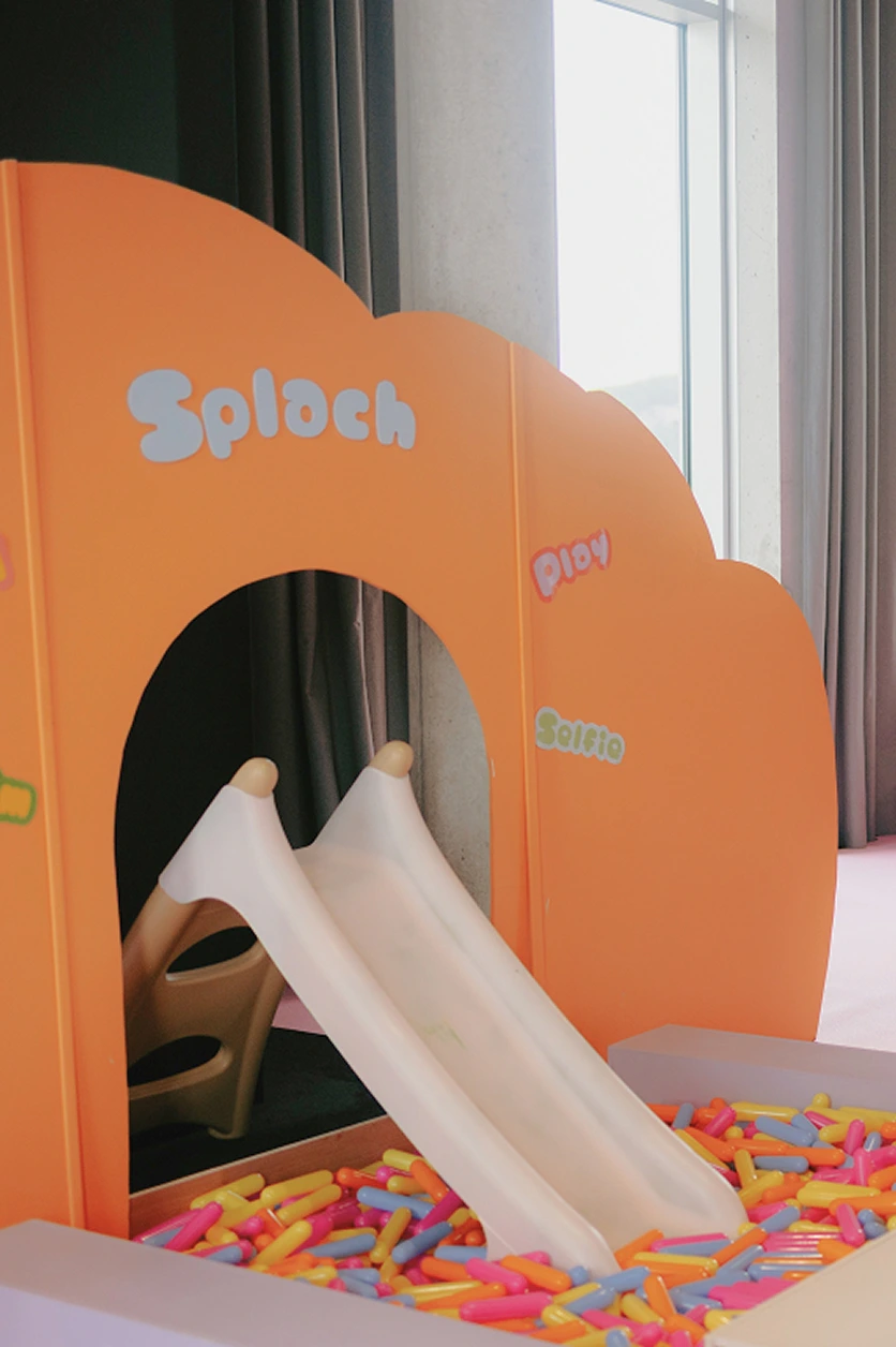 scenographie-espace-jeux-enfants-toboggan-yma Espace de jeux immersif pour enfants avec toboggan blanc, piscine à balles multicolores et décor orange personnalisé.